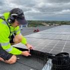 En montör från Nordic Solar monterar nya solceller och fågelskydd på ett stort fastighetstak. Arbetet sker med säkerhetssele, och panelerna läggs i jämna rader för maximal effekt. Pressbild: Nordic Solar