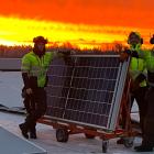 Bilden visar tre montörer som arbetar med installationen av solpaneler på taket vid Solar Sveriges logistikcentrum. De står bredvid en vagn med solpaneler medan himlen bakom dem lyser i intensiva orangea och röda toner från solnedgången. Pressbild: Nordic Solar