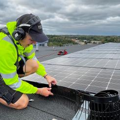 En montör från Nordic Solar monterar nya solceller och fågelskydd på ett stort fastighetstak. Arbetet sker med säkerhetssele, och panelerna läggs i jämna rader för maximal effekt. Pressbild: Nordic Solar
